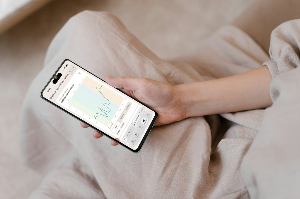 Vrouw houdt een telefoon vast met de symptoomgrafiek van PMDD Tracker, zittend in linnen kleding.